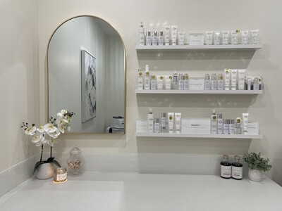 Skincare display at SolSkinn Medical Aesthetics featuring AlumierMD products on floating shelves beside a mirror and orchid arrangement.